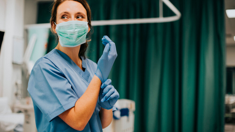 Weibliche Krankenschwester mit Maske zieht Handschuhe an