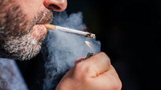 Close up of bearded man holding a lighter and smoking a cigarette on black background