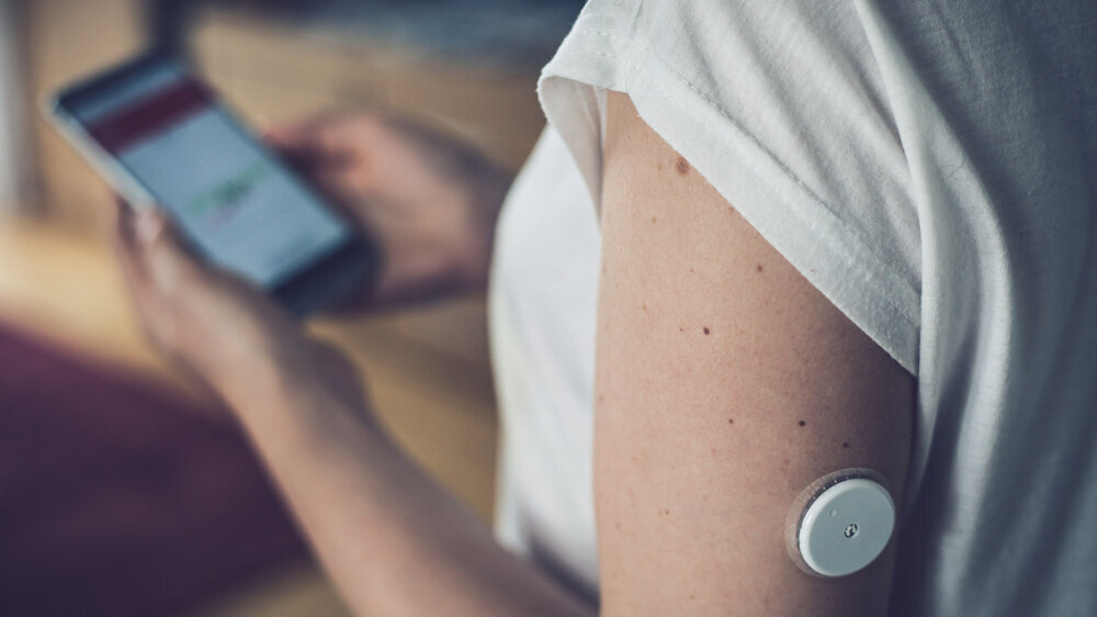 Woman checking glucose level with new technology remote sensor and mobile phone, checkup glucose levels without blood. Diabetes treatment. Focus on foreground. Symbolbild Diabetespatient