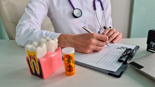Female dentist works on dental implant and writes prescription for dental pills. Tablets for relieving toothache