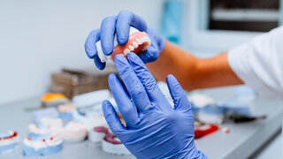 Dental prosthesis, prosthetics work. Close up of prosthetic's hands while working on the denture. Selective focus.