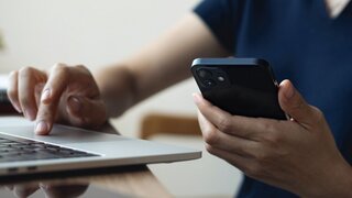 Asian business woman using smartphone, working on laptop computer at coffee shop or home office. Casual woman using smartphone and laptop browsing the internet at cafe, remote work, vertical