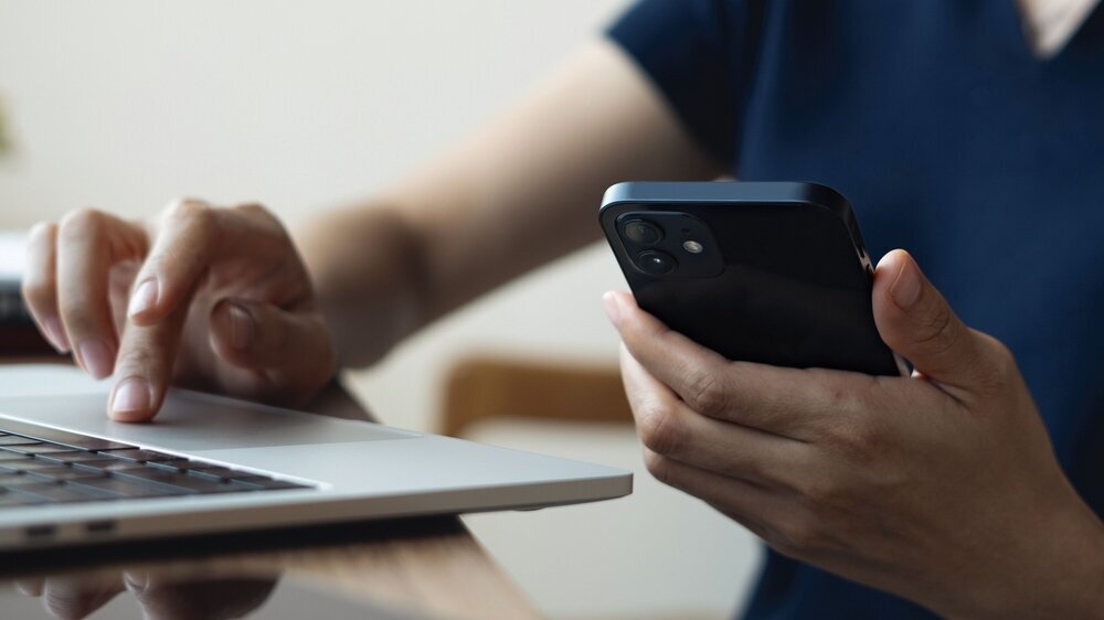 Asian business woman using smartphone, working on laptop computer at coffee shop or home office. Casual woman using smartphone and laptop browsing the internet at cafe, remote work, vertical