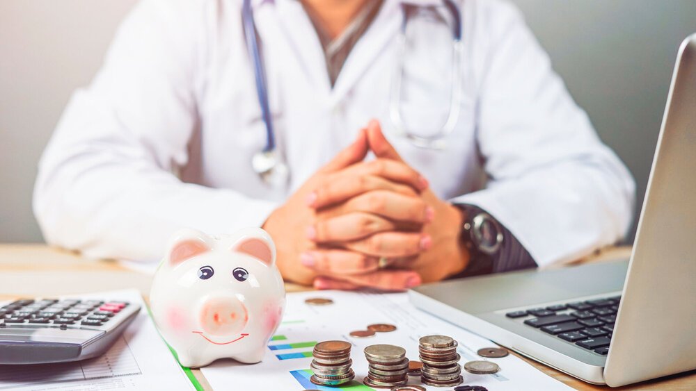 Arzt sitzt im Behandlungszimmer am Schreibtisch und rechnet die Aufwendungen durch.