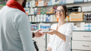 Junge Apothekerin, die dem männlichen Kunden, der an der Kasse des Apothekengeschäfts steht und ein Medikament überreicht.