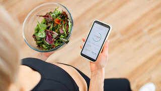 Frau auf einer Waage schaut auf Gesundheits-App