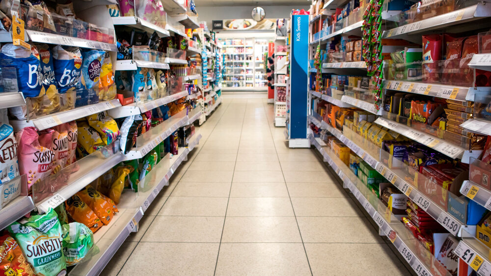 Grocery store aisle showing crisps, biscuits and snacks. Nobody in shot Britischer Supermarkt mit Regalen von Produkten mit hohem Fett-, Salz- und Zuckergehalt.