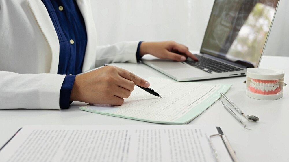 Zahnärztin sitzt am Schreibtisch und prüft ein Schriftdokument.