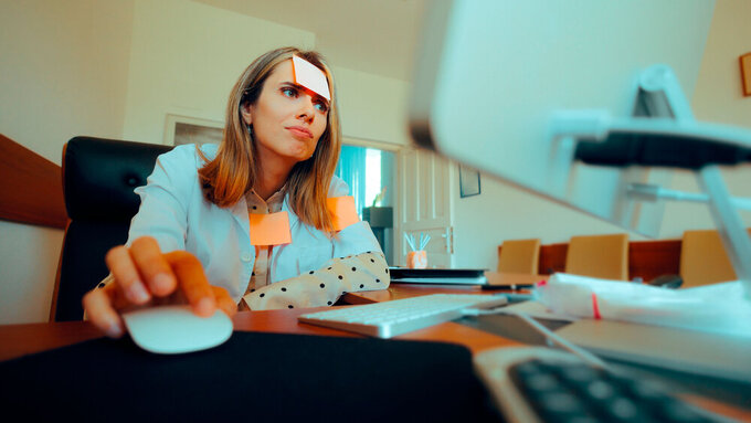 Ärztin sitzt an chaotischem Schreibtisch und versinkt in Bürokratie.
