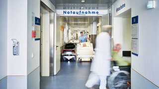 Notaufnahme Eingang Krankenhaus mit Arzt Rollstuhl und Patient in Bewegungsunschärfe auf dem Flur und Pfleger mit Krankenbett
