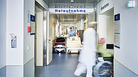 Notaufnahme Eingang Krankenhaus mit Arzt Rollstuhl und Patient in Bewegungsunschärfe auf dem Flur und Pfleger mit Krankenbett