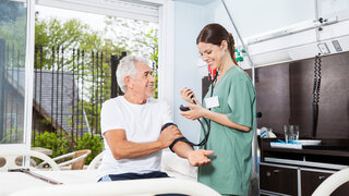 Pflegekraft misst Blutdruck bei älterem Patienten
