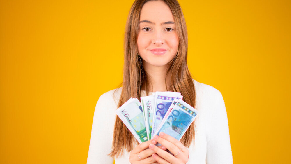 Young beautiful caucasian girl smiling holding money over yellow background
