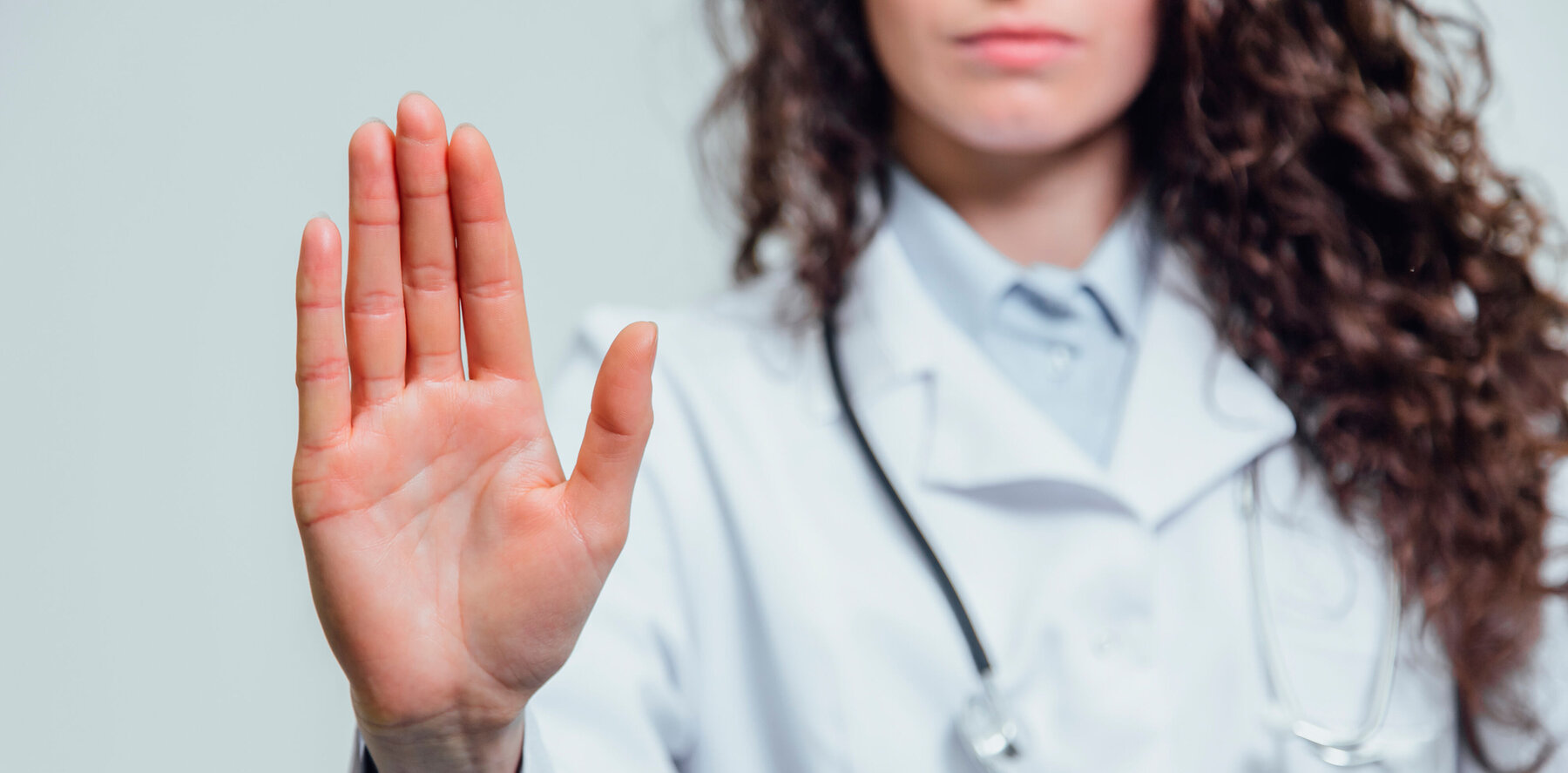Junge Ärztin hält schützend die Hand erhoben, um Gewalt seitens Patienten abzuwehren.