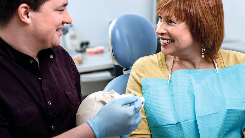 Dentist showing teeth on skull to elder woman patient in the dental office