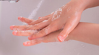 young girl soaped her hands and holds them under the tap in the bathroom in the morning