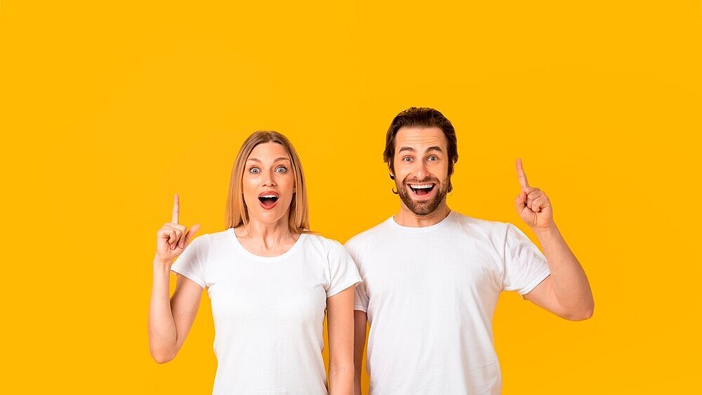 Happy Mixed Gender Couple Smiling And Pointing Upward, Yellow Background, Excitement Concept Excited Happy Mixed Gender Couple Smiling And Pointing Upward At Yellow Background, Engaging In Playful Communication, Capturing Joyful Emotion Expressing Enthusiasm In Studio Setting.