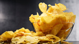 Composition with bowl of potato chips on wooden table.