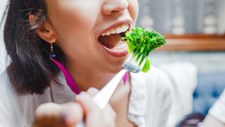 Portrait of happy smiling young casual woman eating broccoli in restaurant