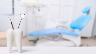 Oral dental hygiene. Healthy white tooth and dentist mirror with explorer probe instrument against blurred dentist Office background with dental chair.