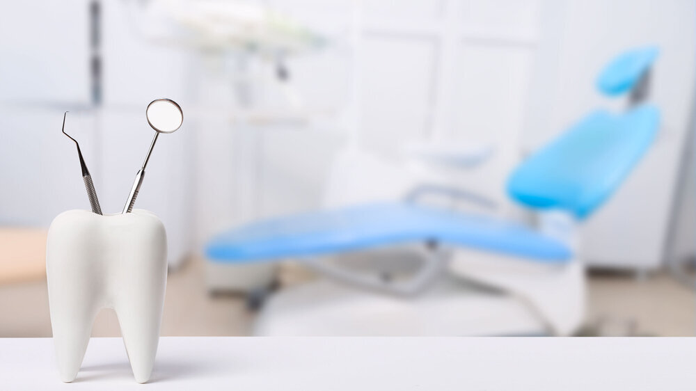 Oral dental hygiene. Healthy white tooth and dentist mirror with explorer probe instrument against blurred dentist Office background with dental chair.