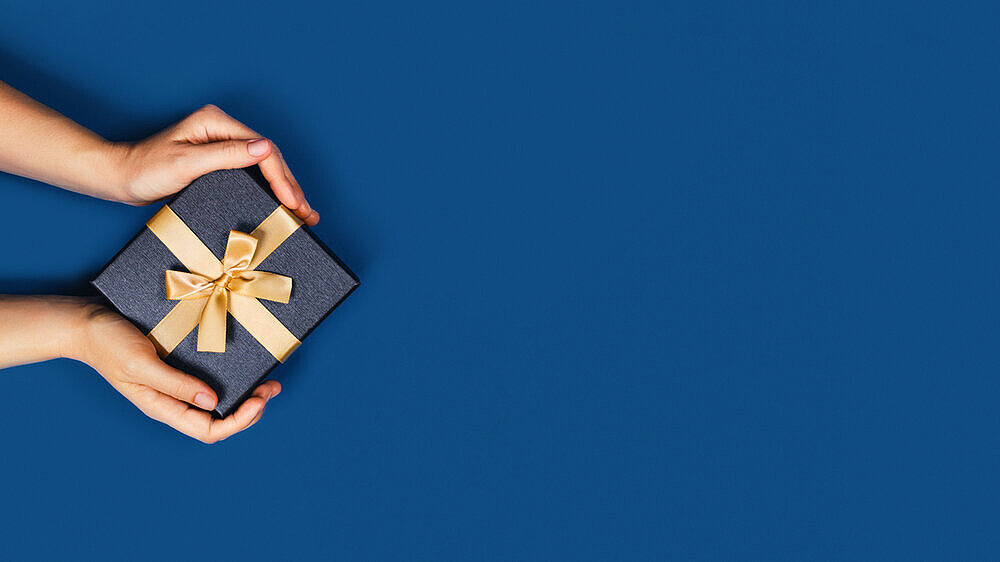 Web-banner with gift box in a female hands on classic blue background. Flat lay, top view, place for text.