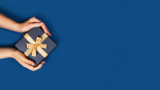 Web-banner with gift box in a female hands on classic blue background. Flat lay, top view, place for text.