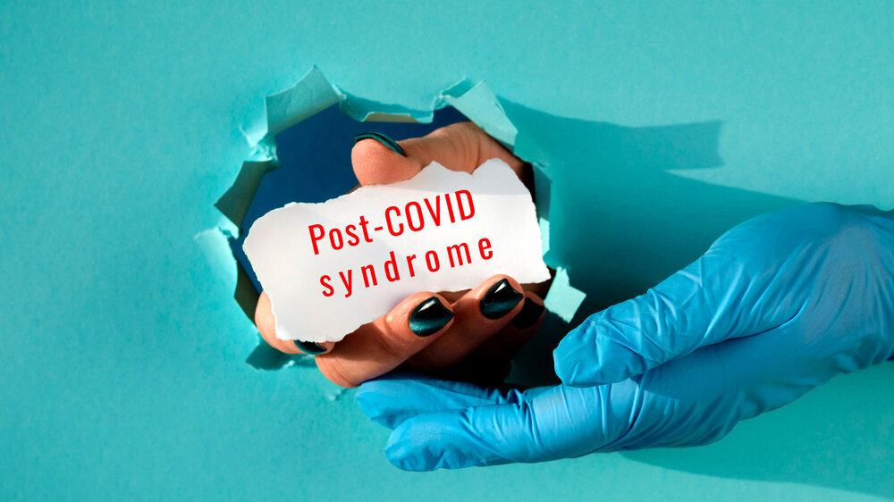Post Covid syndrome, long covid. Hand in glove supporting hand with text on scrap of paper in paper hole. Long COVID