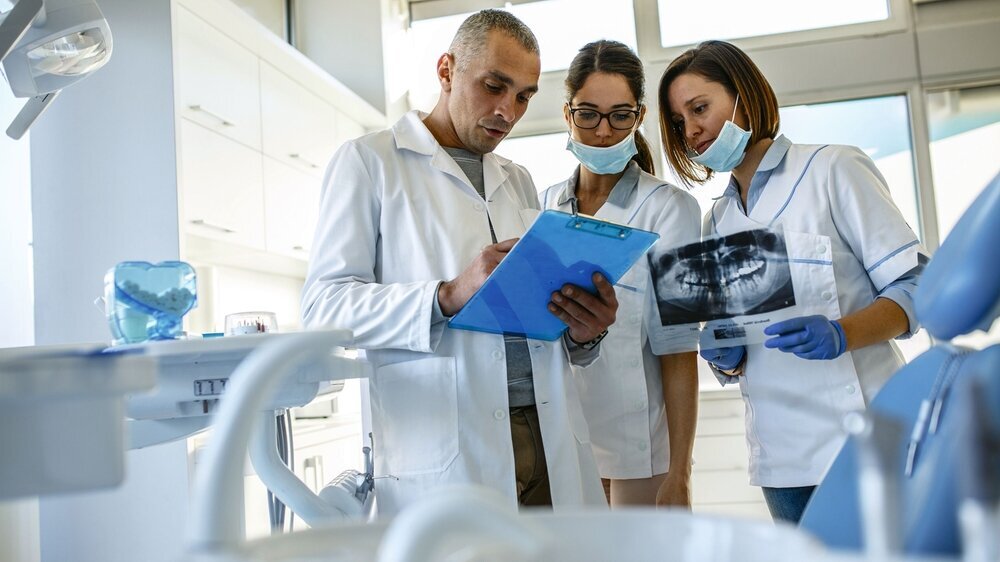 Gruppe von Zahnärzten, die Röntgenbilder von Patientenzähnen untersuchen. Stehend in neuen hellen Zahnarztpraxis.