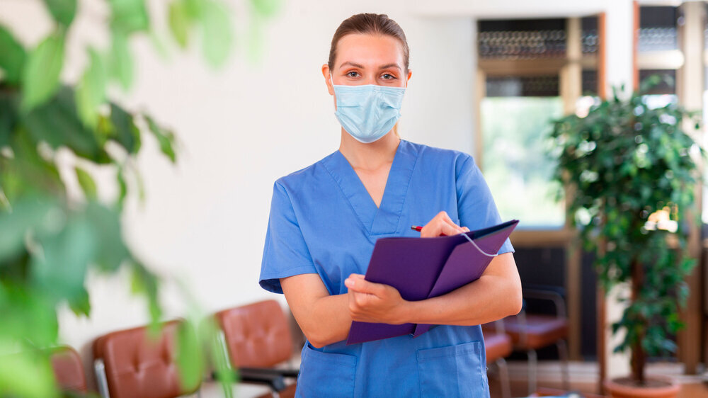 Arzthelferin mit Gesichtsschutzmaske steht in einer Arztpraxis Bis zum 7. April 2023 bleibt die Maskenpflicht als letzte Corona-Schutzmaßnahme für PatientInnen und BesucherInnen in Arzt- und Zahnarztpraxen bestehen.