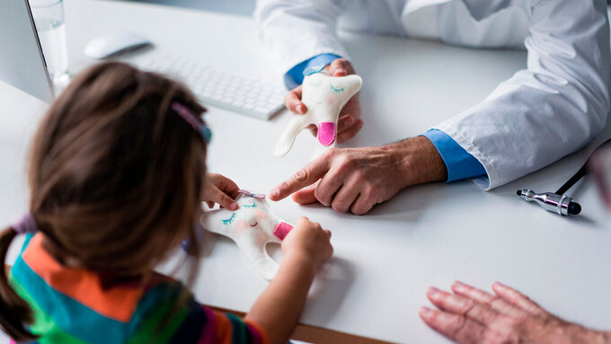 Zahnarzt erklärt Kind Zahnmodell am Schreibtisch