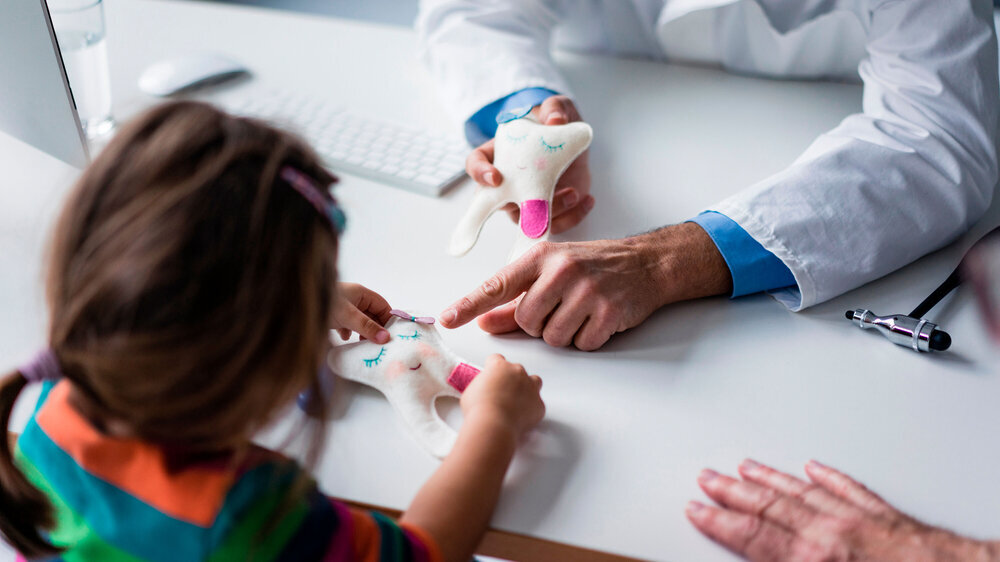 Zahnarzt erklärt Kind Zahnmodell am Schreibtisch