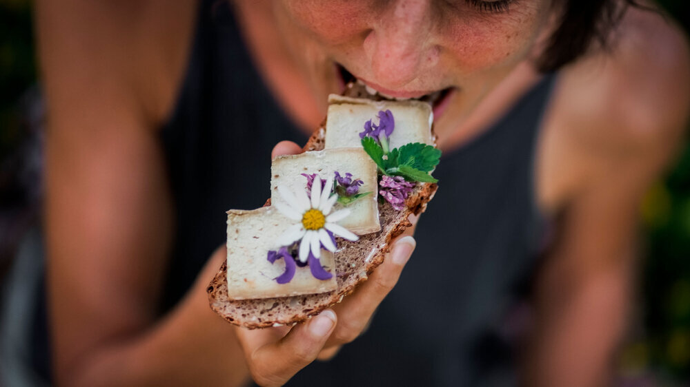 Bird view of a happy woman eating vegan cheese substitute slices on a whole grain bread flowery decorated with daisy for a healthy snack in a green meadow