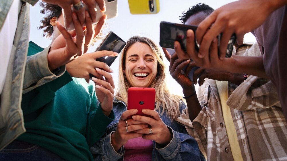 Generation Z: Gruppe junger Teenager mit Smartphones in den Händen. Mittig steht ein blondes Mädchen, das lacht. Generation Z: Gruppe junger Teenager mit Smartphones in den Händen. Mittig steht ein blondes Mädchen, das lacht.