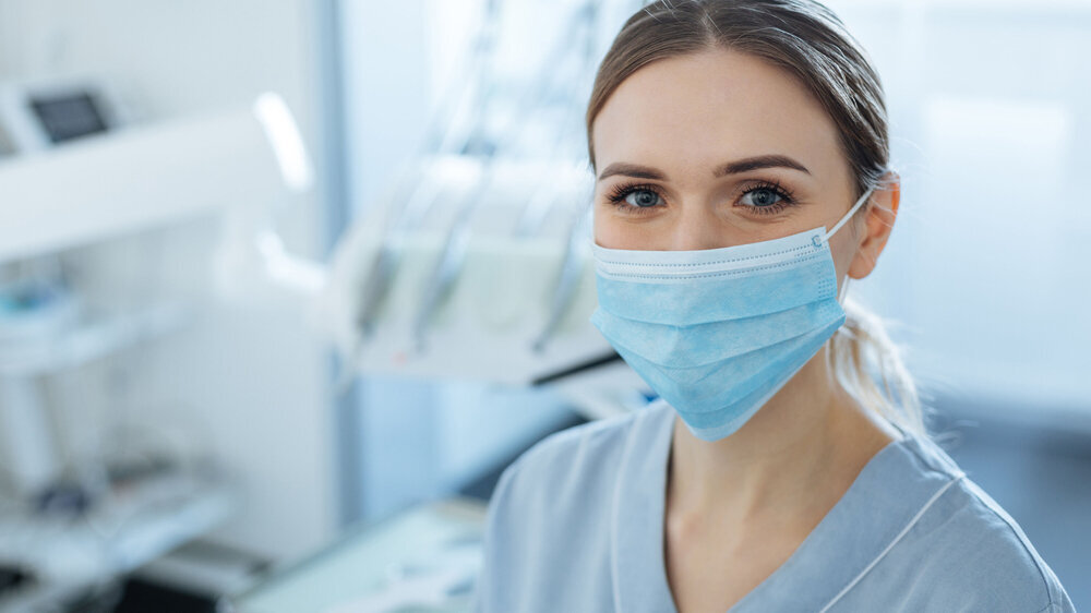 Junge zahnmedizinische Fachangestellte in der Ausbildung, Praxis im Hintergrund.