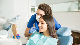 Female dentist showing braces to teenage girl in mirror at dental clinic