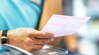 Apotheker hält rosa Arzneirezept in der Hand. Ausstellen von Patientenrezepten.