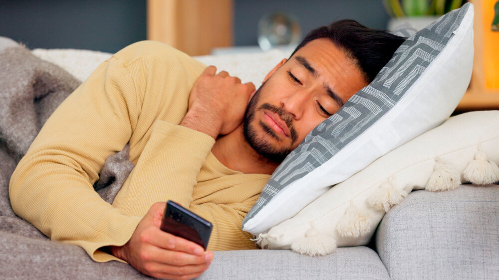 Ein Mann liegt krank auf dem Sofa und hat sein Smartphone in der Hand. Ein Mann liegt krank auf dem Sofa und hat sein Smartphone in der Hand.