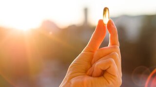 Hand einer Frau hält Fischöl Omega-3-Kapseln, Sonnenuntergang Hintergrund. Gesunde Ernährung, Medizin, Gesundheitsversorgung, Nahrungsergänzungsmittel