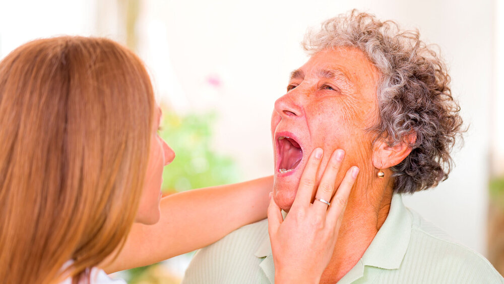 Ärztin untersucht den Mund einer älteren Patientin