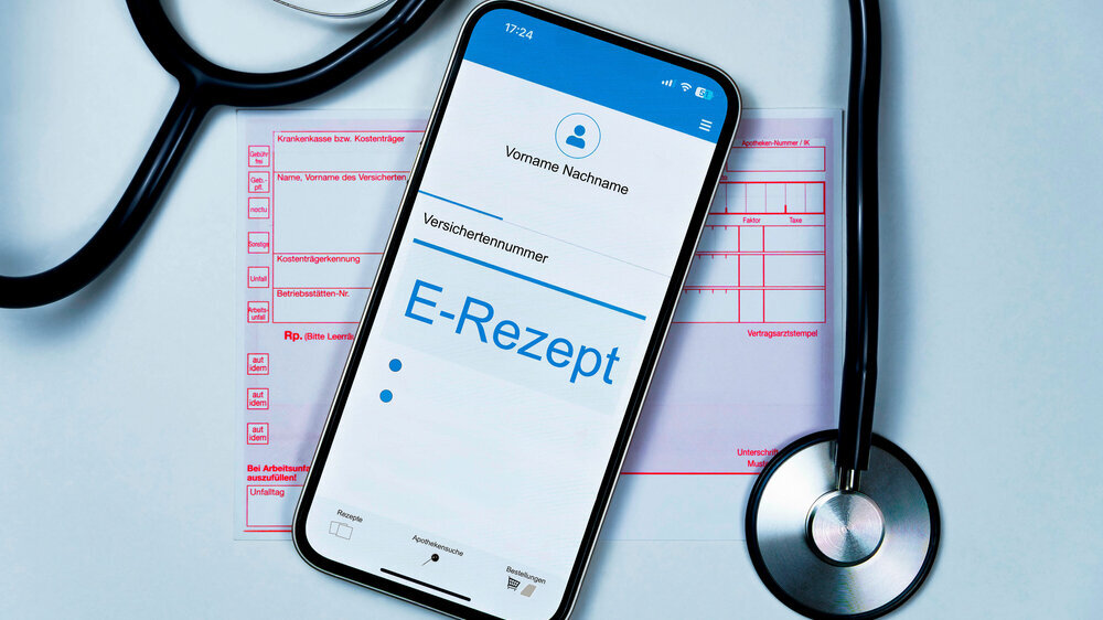 Smartphone mit e Rezept auf dem Display liegt auf herkömmlichen Kassenrezept, ein Stethoskop liegt daneben, horizontal, weißer Hintergrund E-Rezept