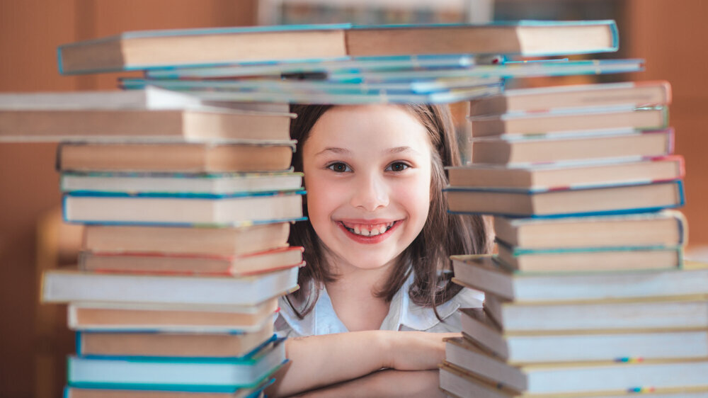 Kind sitzt zwischen Bücherstapeln und lacht Kind sitzt zwischen Bücherstapeln und lacht