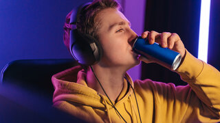 Young professional cybersport gamer playing online video game late at night, drinking caffeine energy drink to wake up and concentrate, focus on multiplay tournament. Games addiction concept