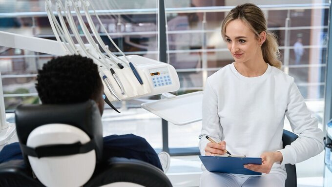 Junge Zahnärztin hört Patienten aufmerksam zu und macht Notizen auf dem Anamnesebogen. Junge Zahnärztin hört Patienten aufmerksam zu und macht Notizen auf dem Anamnesebogen.