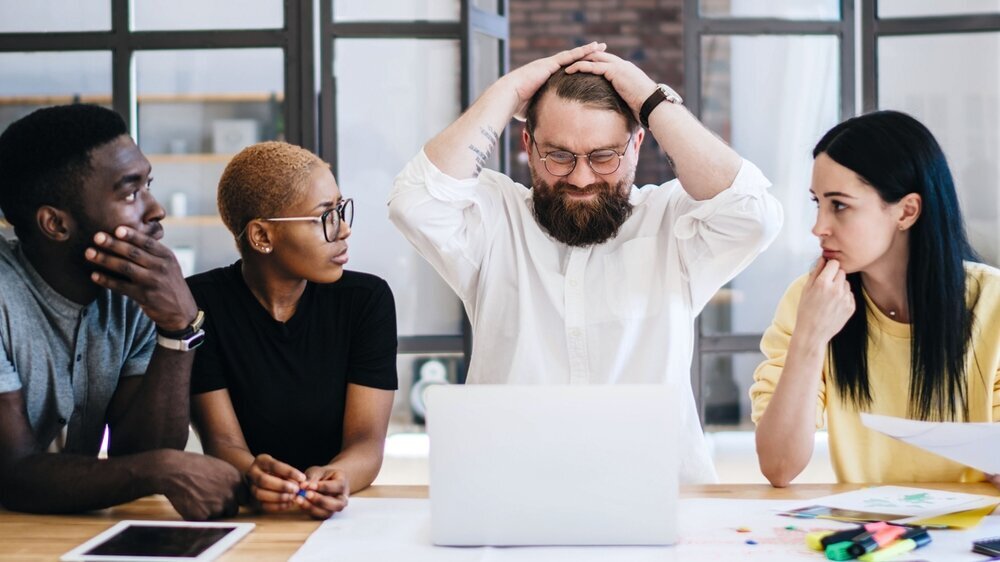 Group of confused multiethnic coworkers using laptop at office Fehler Teambesprechung