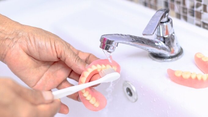 Brush old woman hand to clean denture