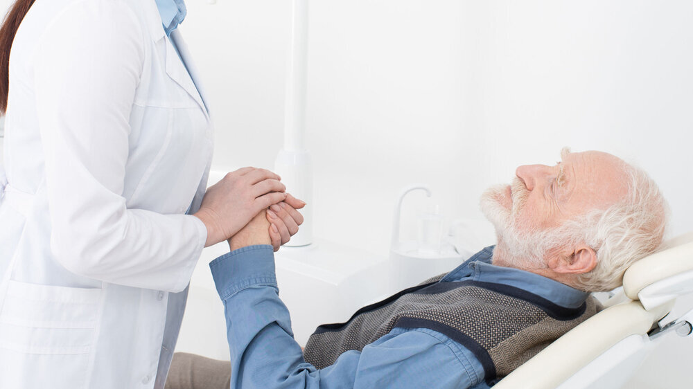 Liegender Patient hält die Hand des Zahnarztes