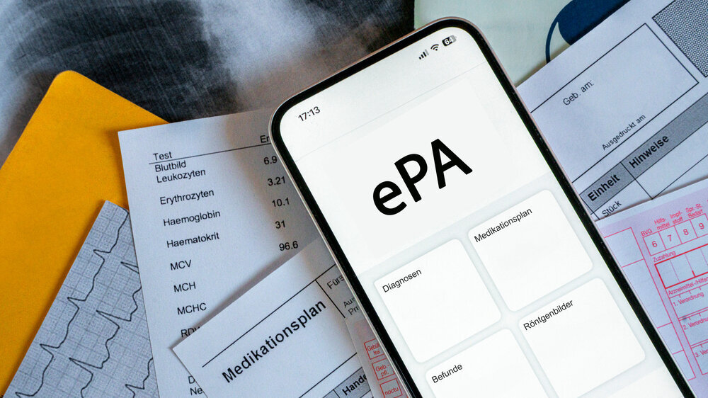 Ein Smartphone auf dem gerade eine elektronische Patientenakte angezeigt wird, liegt auf medizinischen Dokumenten, horizontal Ein Smartphone auf dem gerade eine elektronische Patientenakte angezeigt wird, liegt auf medizinischen Dokumenten, horizontal