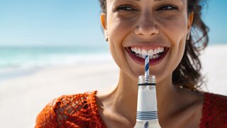 Junge glückliche Frau trinkt Softdrink am Strand