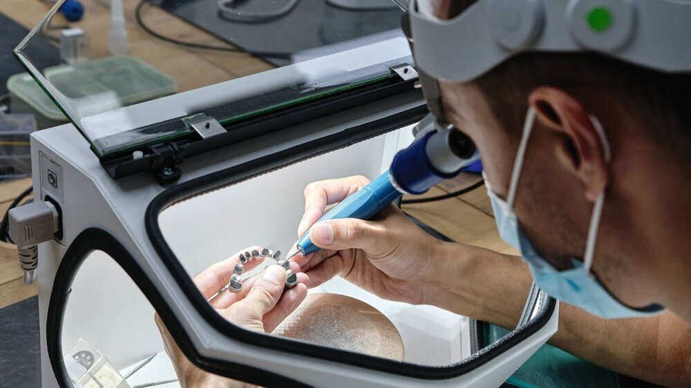 Dentist hand mills tooth crowns created on 3d printer for metal. Dental technician working with ceramic crowns in protective box at the laboratory. Zahntechniker